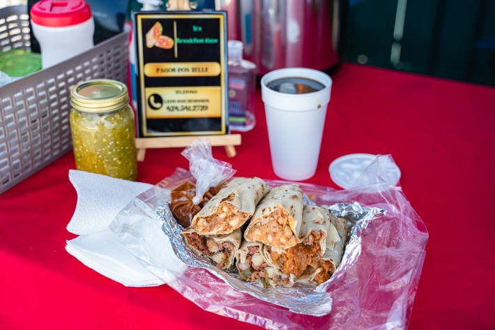 A jar of green salsa, next to burritos and a cafe de olla.