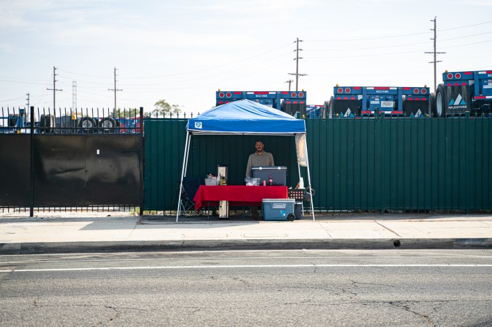 A blue tent over a red table with a street vendor standing in the middle