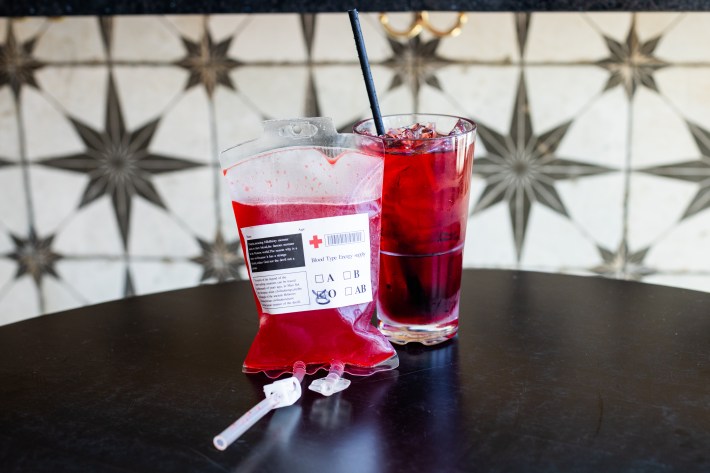 A red cocktail served with an I.V. bag full of red liquid.