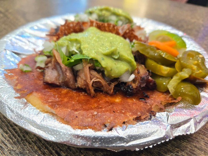 A carnitas taco with a big dollop of guacamole on top and pickled jalapenos and carrots on the side