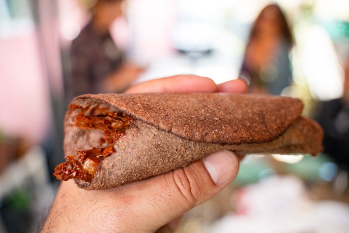 A taco de barbacoa de res on a red corn tortilla.