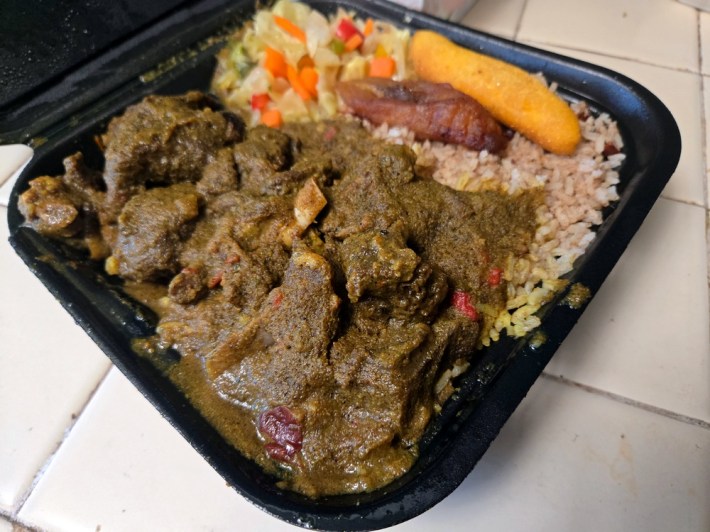 A to-go container of Jamaican-style curry goat, with rice and plantains