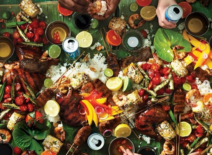 A messy, banana leaf-strewn table covered with food, meats, vegetables, fruits, and drinks.