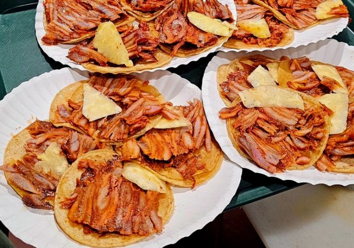 Paper plates filled with tacos al pastor topped with pineapple