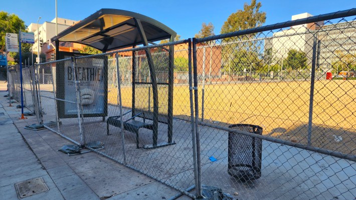 A chainlink fence blocks a Metro bus shelter on 1st Street between Spring Street and Broadway.