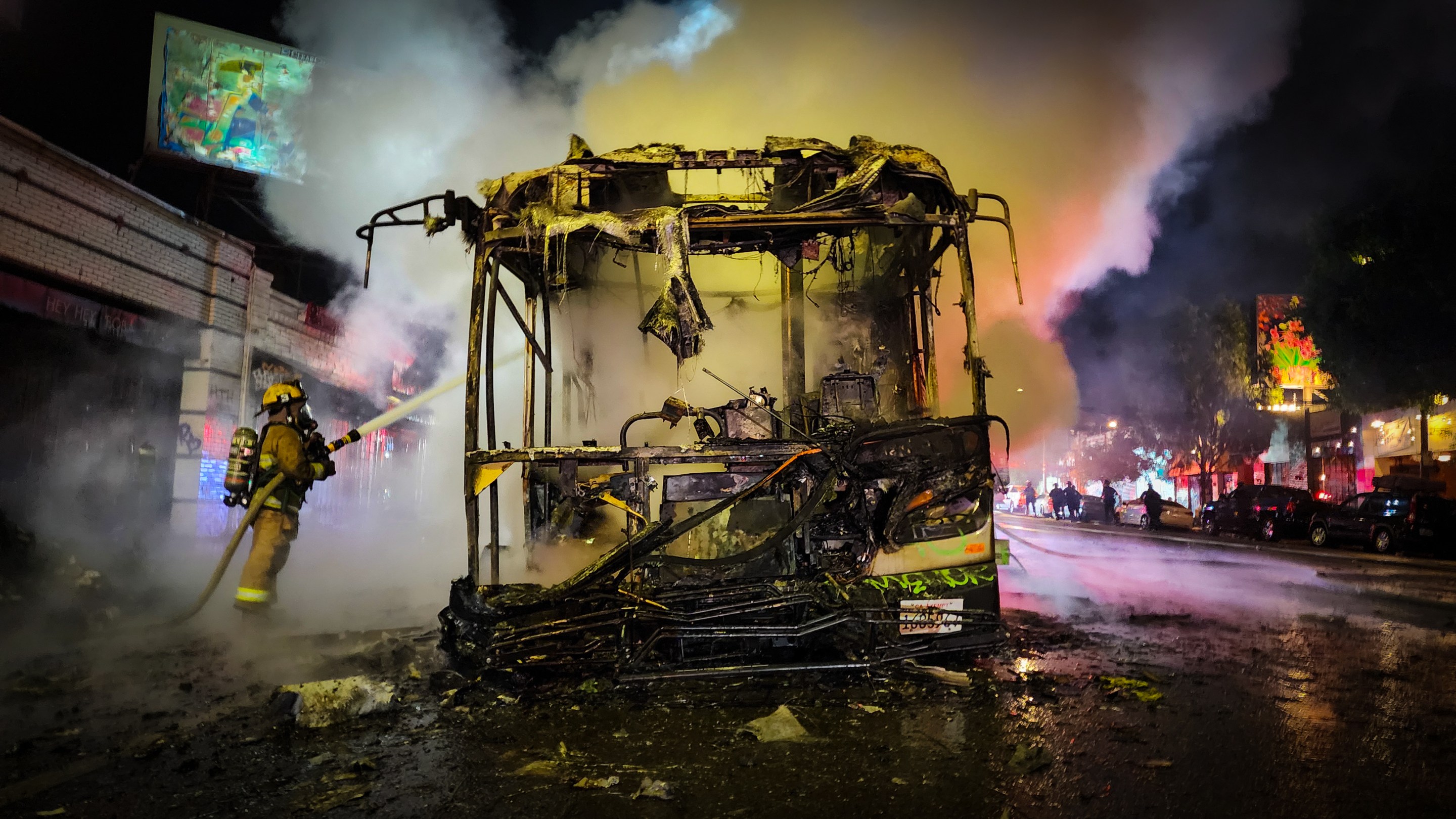 A Los Angeles firefighter stands on the right side of charred Metro bus. The firefighter exstinguishes a fire that started on a Metro bus after someone lit off a firework inside of the vehicle. Smoke emenates from the bus.