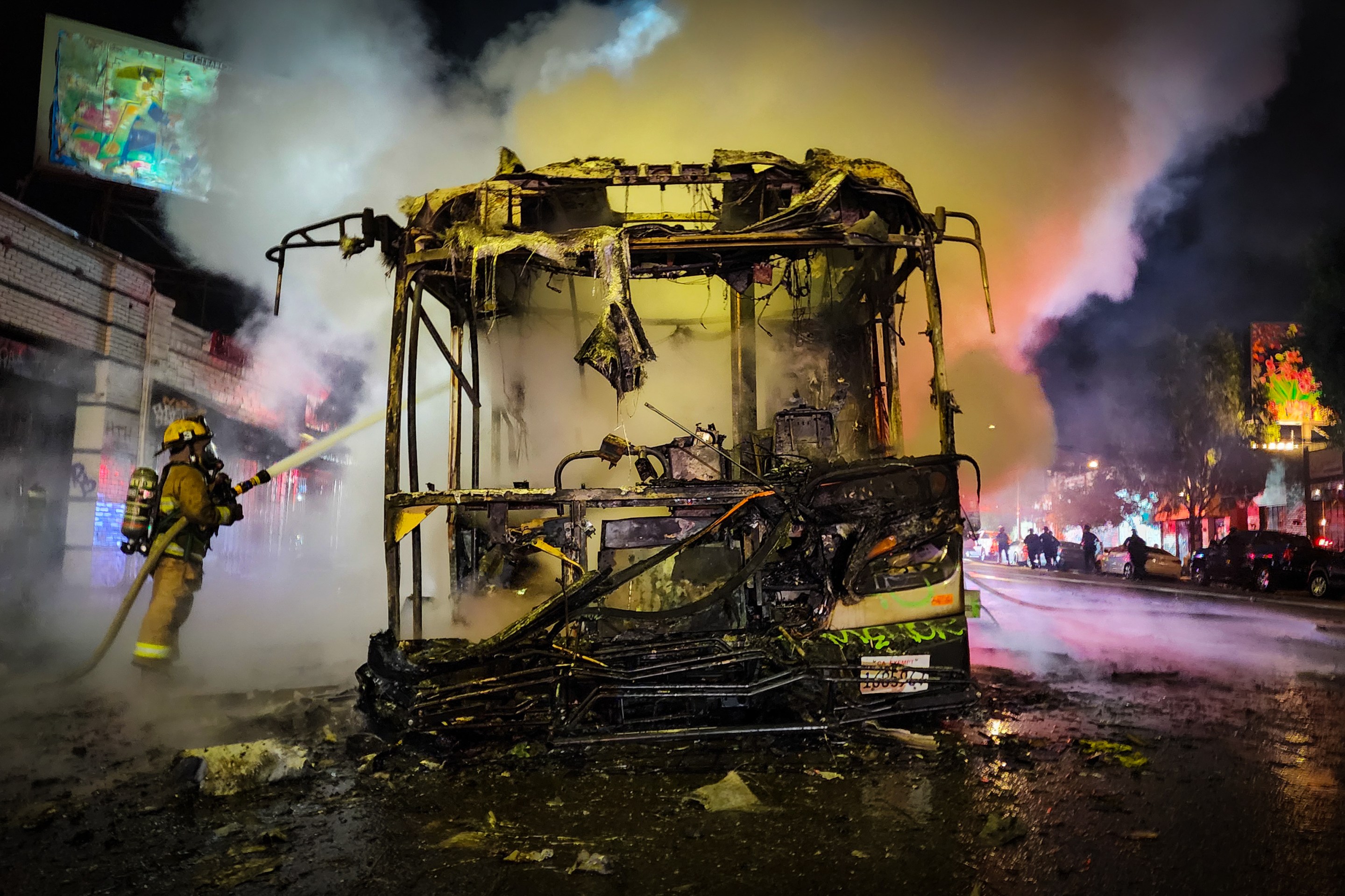 A Los Angeles firefighter stands on the right side of charred Metro bus. The firefighter exstinguishes a fire that started on a Metro bus after someone lit off a firework inside of the vehicle. Smoke emenates from the bus.