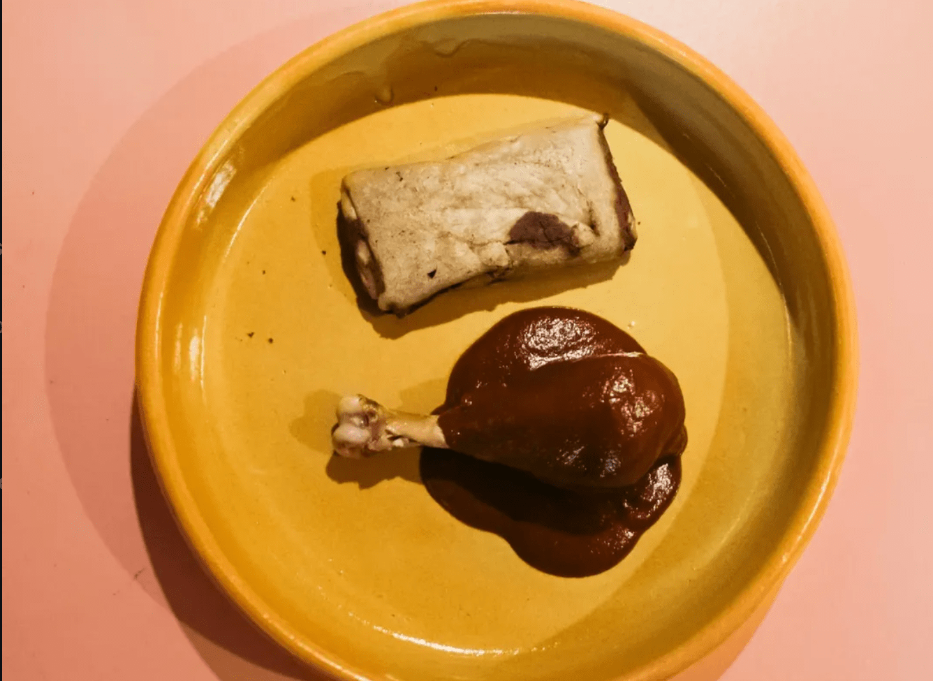 Mole tamal on a yellow plate next to a mole-covered chicken leg.
