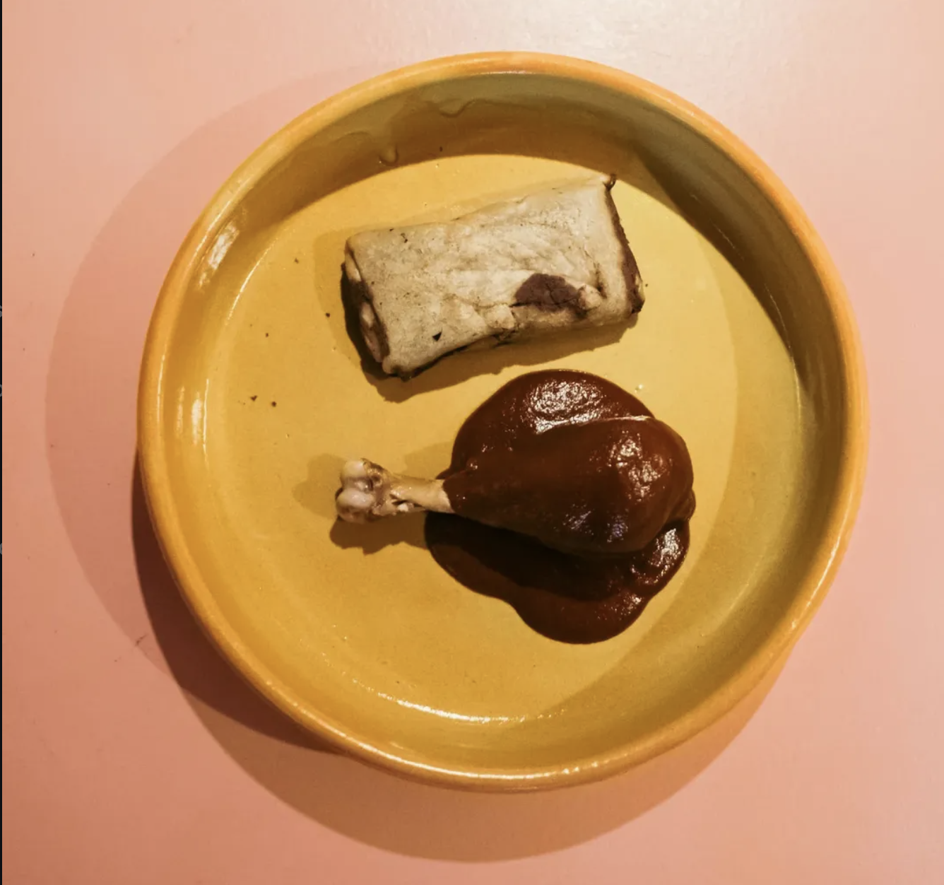 Mole tamal on a yellow plate next to a mole-covered chicken leg.