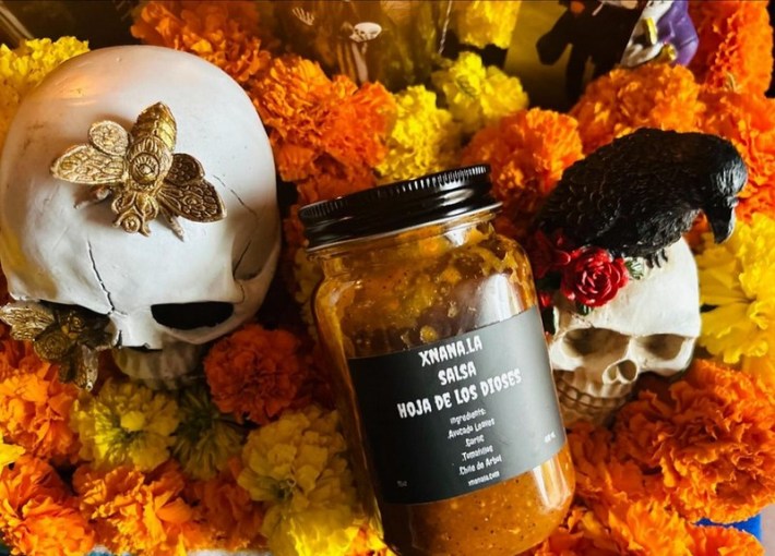 Xnana's Salsa Hoja De Los Dioses on a background of marigolds and skulls.