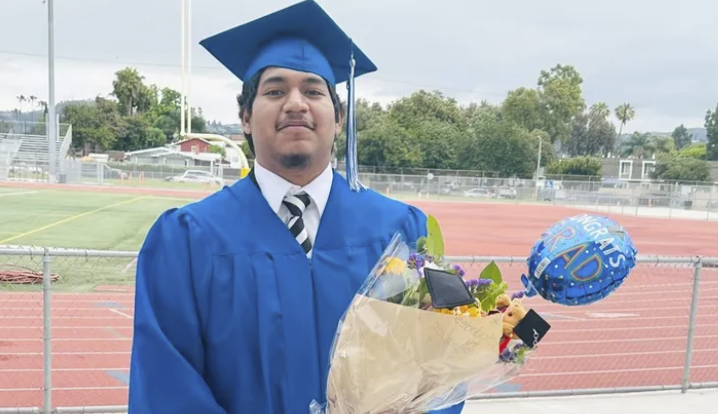 Imanol Salvador Gonzalez stands in a cap and gown holding a bouquet of flowers.