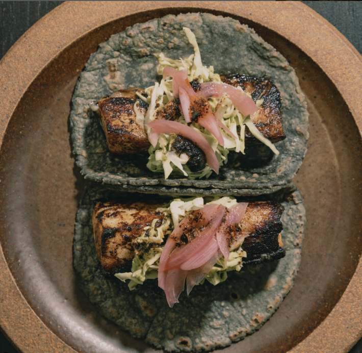 A seared fish taco topped with cabbage and pickled red onions.