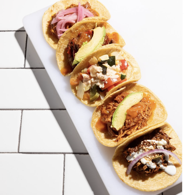 Five assorted tacos de guisados are lined on a plate.