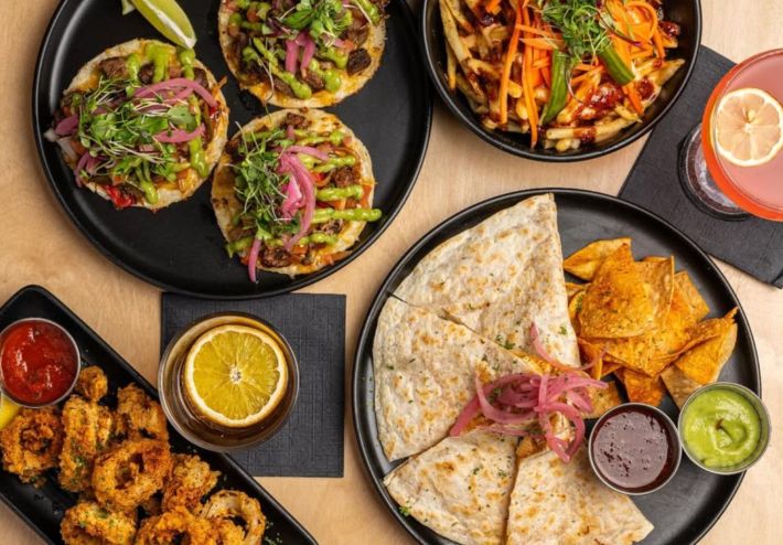 A food spread of tacos, quesadilla, loaded fries and crispy onion rings.