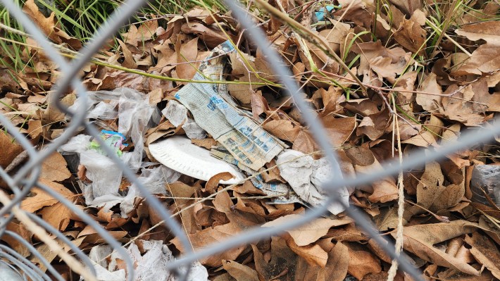 A close up of trash and dead leaves looking through the chain link fence.