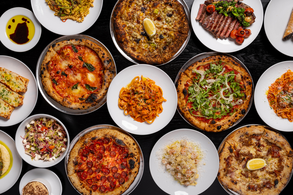 A huge arrangement of pasta, pizza, fish, steak, and salads at Downtown Dough on a black background.