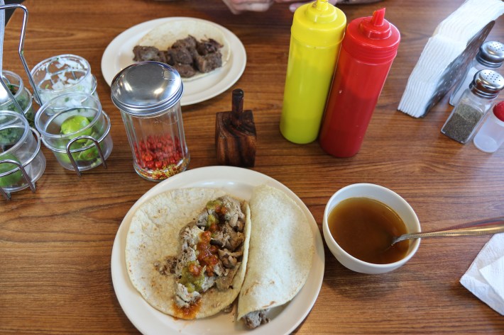 Tacos de sesos (brain tacos) topped with red and green salsa and consomé on the side.