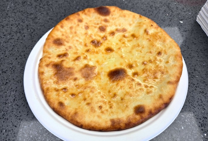 A round, bread-based Imeruli khachapuri, glistening with butter and spotted from cooking, and at Saqartvelo.