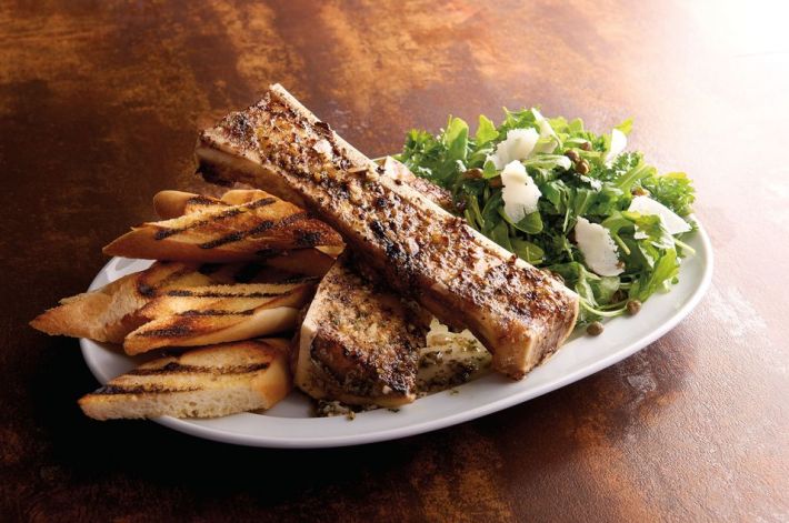 Two large bones with marrow over bread next to a salad with flakes of Parmesan cheese