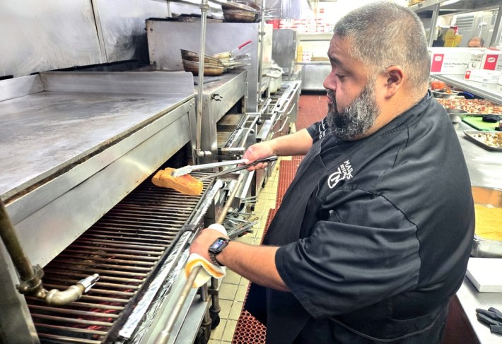 Chef Walter Mayen putting a steak on the grill at Mastro's, using tongs.