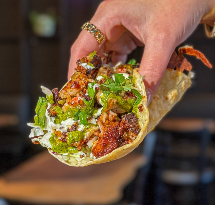 A taco revolcado from El Coraloense is filled with marinated mahi mahi al pastor that is grilled to perfection and served with a side of fresh cabbage, taco cream, and zesty green sauce for the perfect balance of flavor.