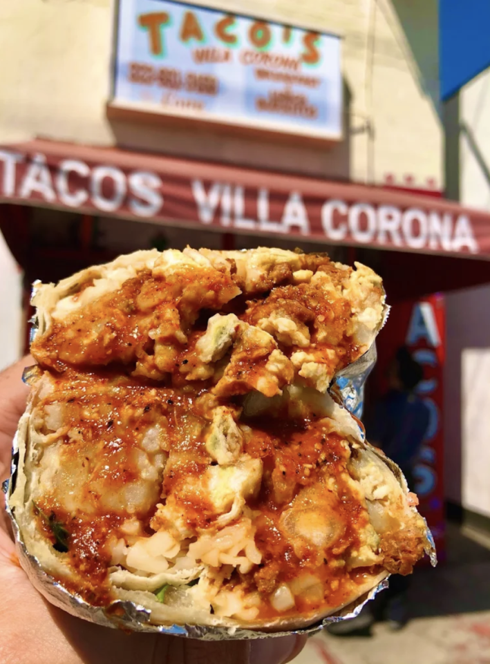 A potato breakfast burrito cut in hald with red salsa poured over it.