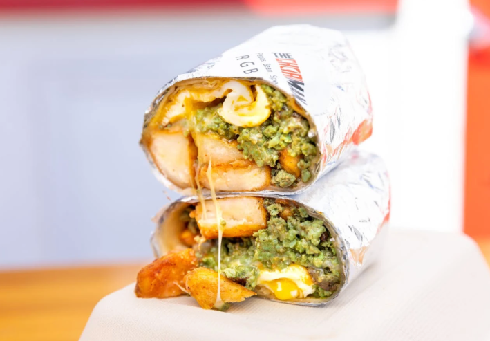 Green chorizo breakfast burrito sliced in half with melty cheese and yolk bursting at the seems.