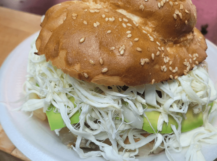 A large cemita poblana with overflowing cheese and slices of avocado on a sesame- seed spotted roll.
