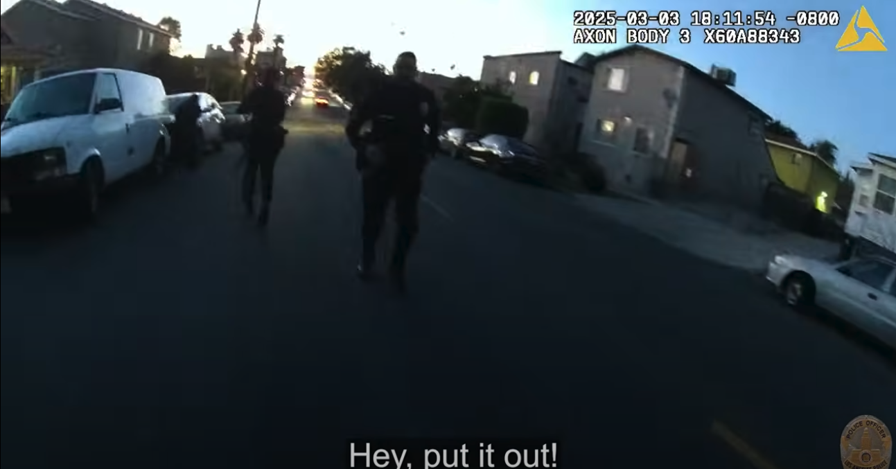 A screenshot from the the body camera footage that LAPD released of the Hector Alaniz shooting. Two LAPD officers stand in the street while one says "Hey, put it out!"