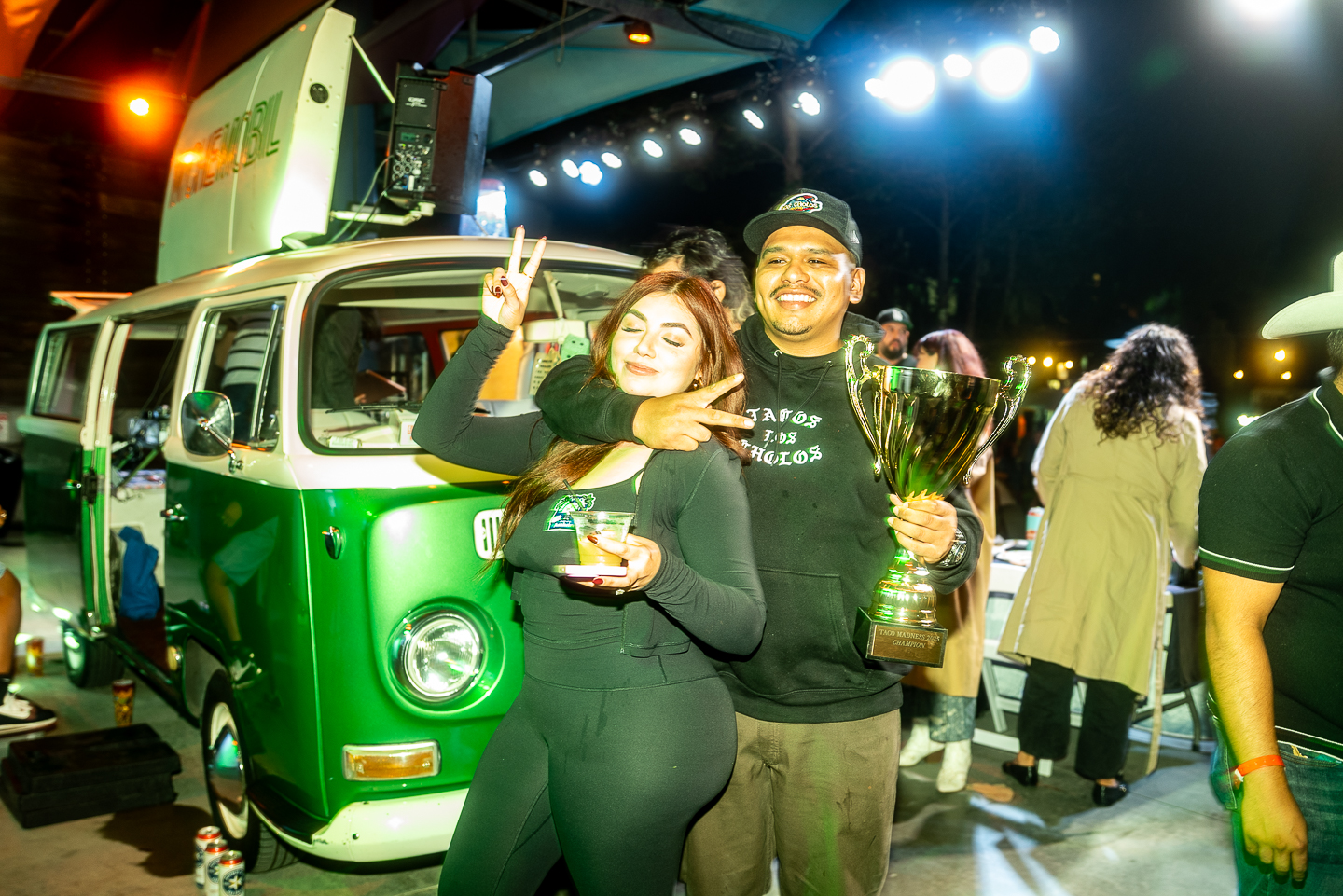 A woman and man hold up a trophy in front of a Volkwagen bus.