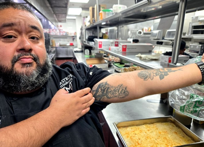 A bearded chef shows off his Los Angeles tattoo with a rolled up sleeve, next to a tattoo of a rose.