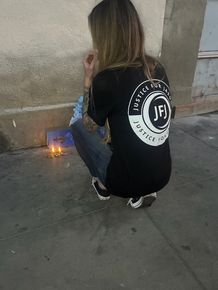 Alex Smith sets up a memorial for her husband in Skid Row. Two candles burn as Smith crouches down with her back to the camera. She's wearing a "justice for Jason" t-shirt.