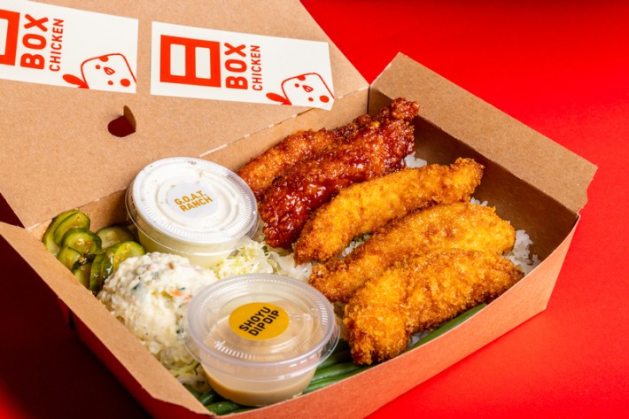 A box meal of five chicken tenders, with containers of shoyu dip, ranch, and sides of pickles and coleslaw, in a cardboard box