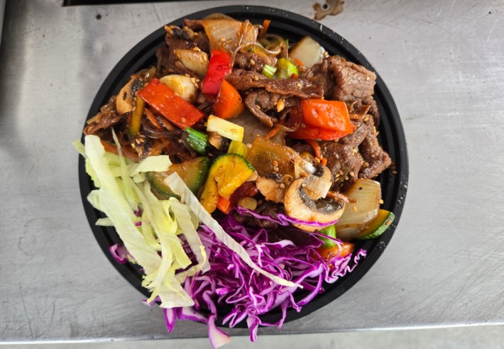 A black pastic bowl of bulgogi, vegetables, and glass noodles at Assa.