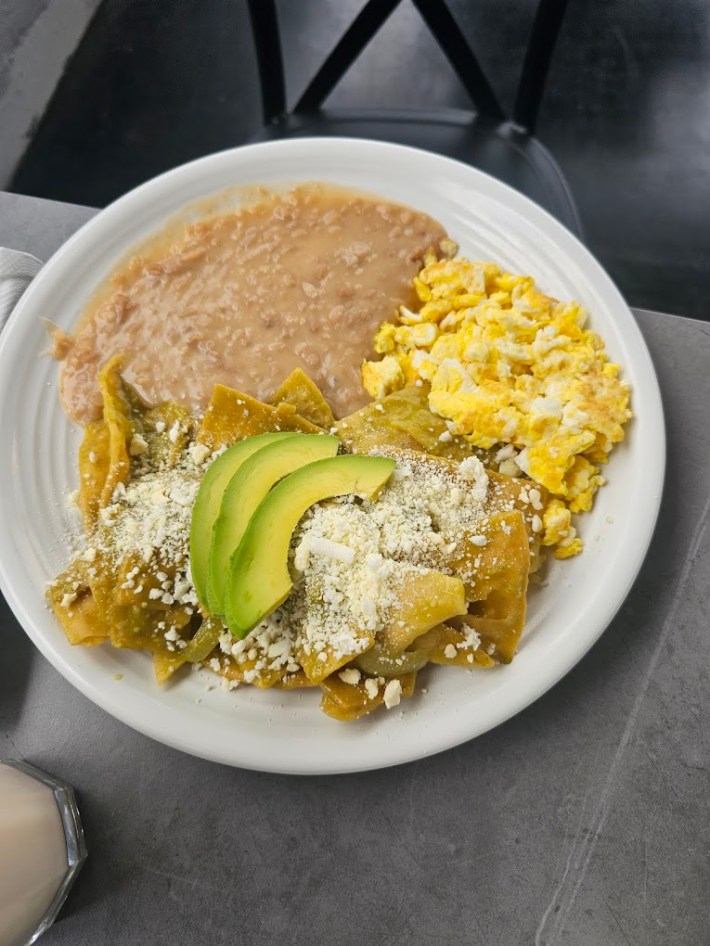 green chilaquiles topped with cheese, and avocado next to scrambled eggs and refried beans.