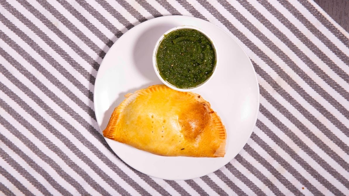 An empanada with pebre sauce, a traditional Chilean sauce made to pour over the empanada’s filling, made with jalapeños, cilantro, green bell peppers, salt, garlic, olive oil, and onions.