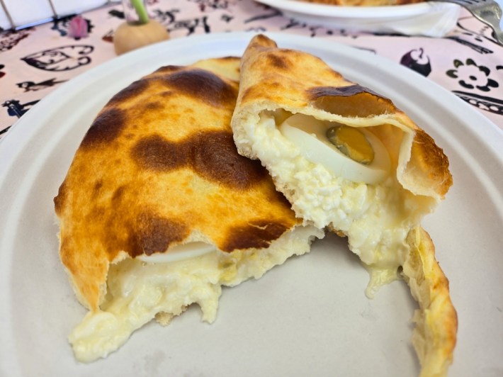 Looking inside a crescent-shaped, bread-based Guiran khachapuri to see its interior of soft cheese and hard-boiled egg at Saqartvelo.