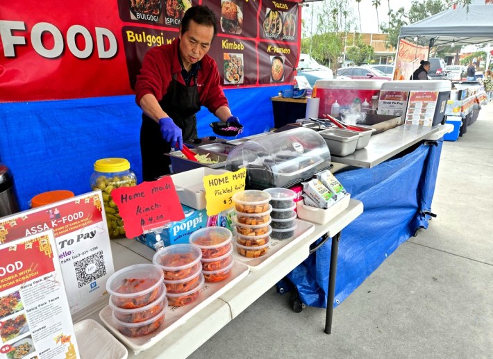 Ken Lee prepares a bulgogi bowl, while offering several varieties of his traditional, homemade kimchi, which is shown in containers at the front of his service table.