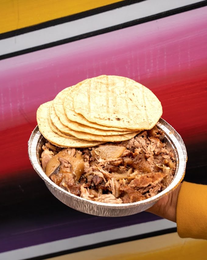 A plate full of carnitas mixtas with warm tortillas on top.