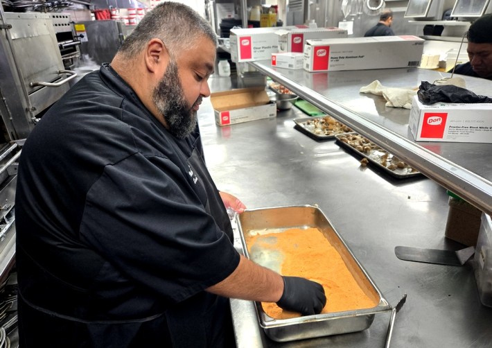 Chef Walter Mayen in black, rubbing a steak in Mastro's light orange-colored secret rub recipe.