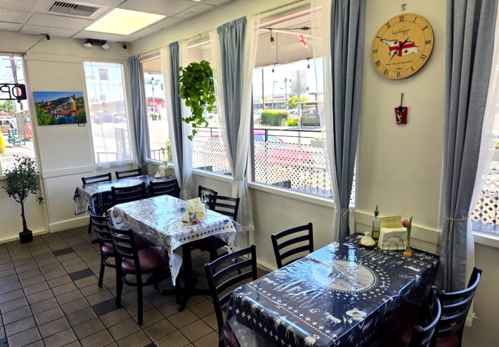 The interior of Saqartvelo Georgian Cuisine in Van Nuys, showing two tables, windows, and a clock-with the shape of Georgia in the center.