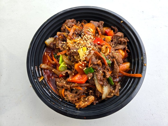 A black pastic bowl filled with spicy pork, vegetables, and Tteokbokki at Assa in Venice.