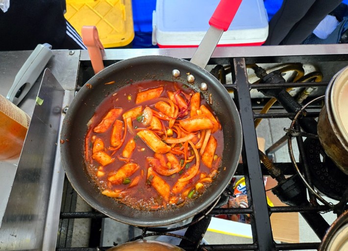Tteokbokki being heated in a pan on a four-burner stove at Assa.