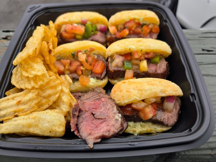 A black plastic tray full of five sandwiches, made with picanha steak and cheese bread, with some potato chips and extra picanha served on the side, at Prime Flavor Brazilian BBQ in Venice.