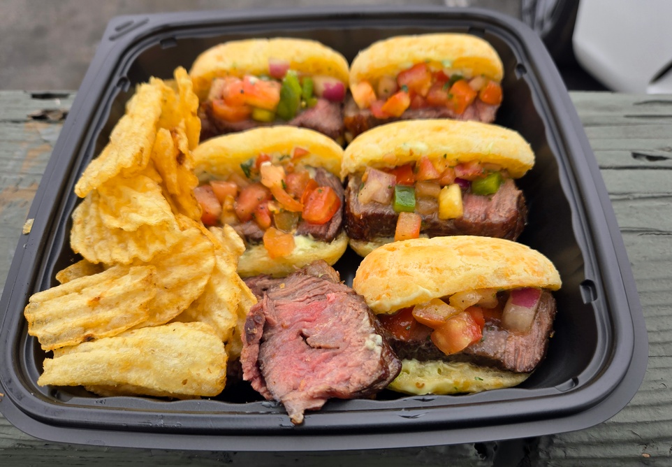 A black plastic tray full of five sandwiches, made with picanha steak and cheese bread, with some potato chips and extra picanha served on the side, at Prime Flavor Brazilian BBQ in Venice.