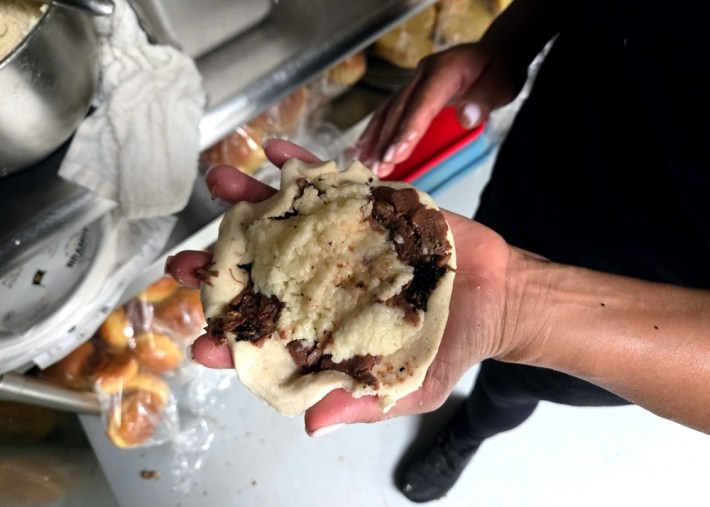 An open hand holding a pupusa that is yet to be folded, showing cheese and brisket.