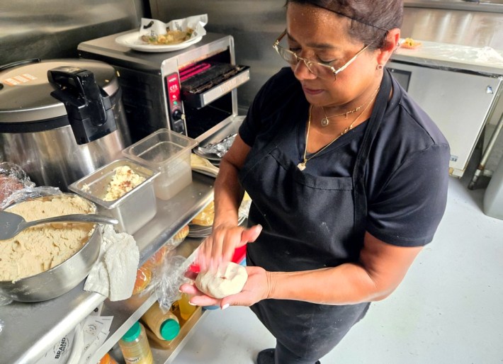 Anabell Ramirez, in a blue apron, glasses, and hairnet, hand-making pupusas at Ray's BBQ.
