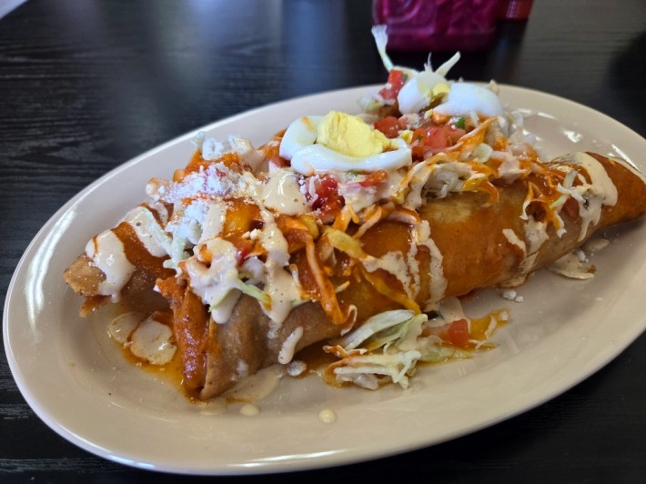 Two Honduran tacos, rolled, fried tacos that resemble Mexican taquitos, covered in chimol, dressing, slices of hard-boiled egg, and cabbage