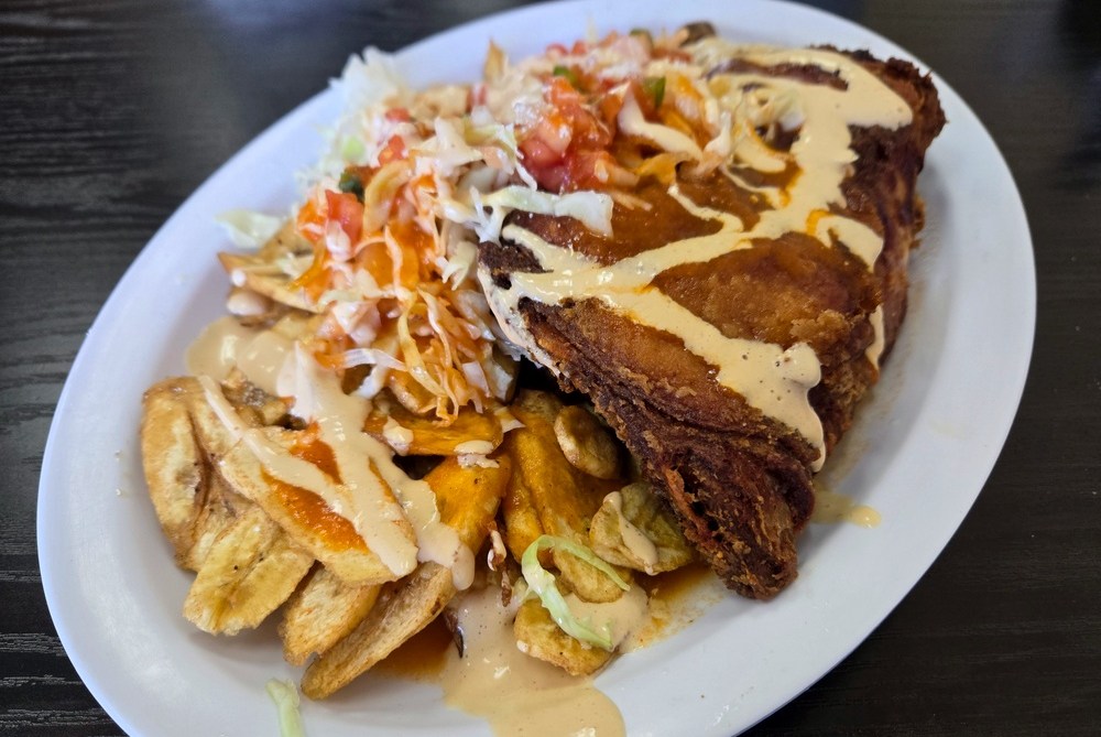 A huge leg and thigh of fried chicken drizzled in light yellow sauce, with plantains and cabbage