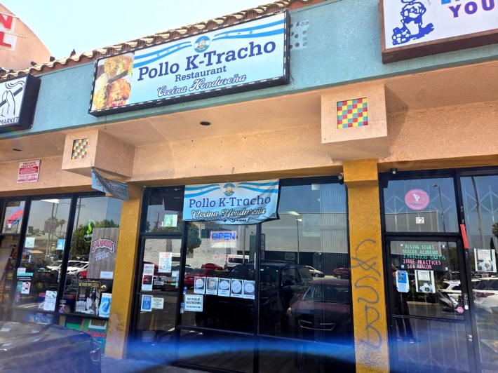 A storefront with a blue and white sign that says Pollo K-Tracho Restaurant Cocina Hondurena.